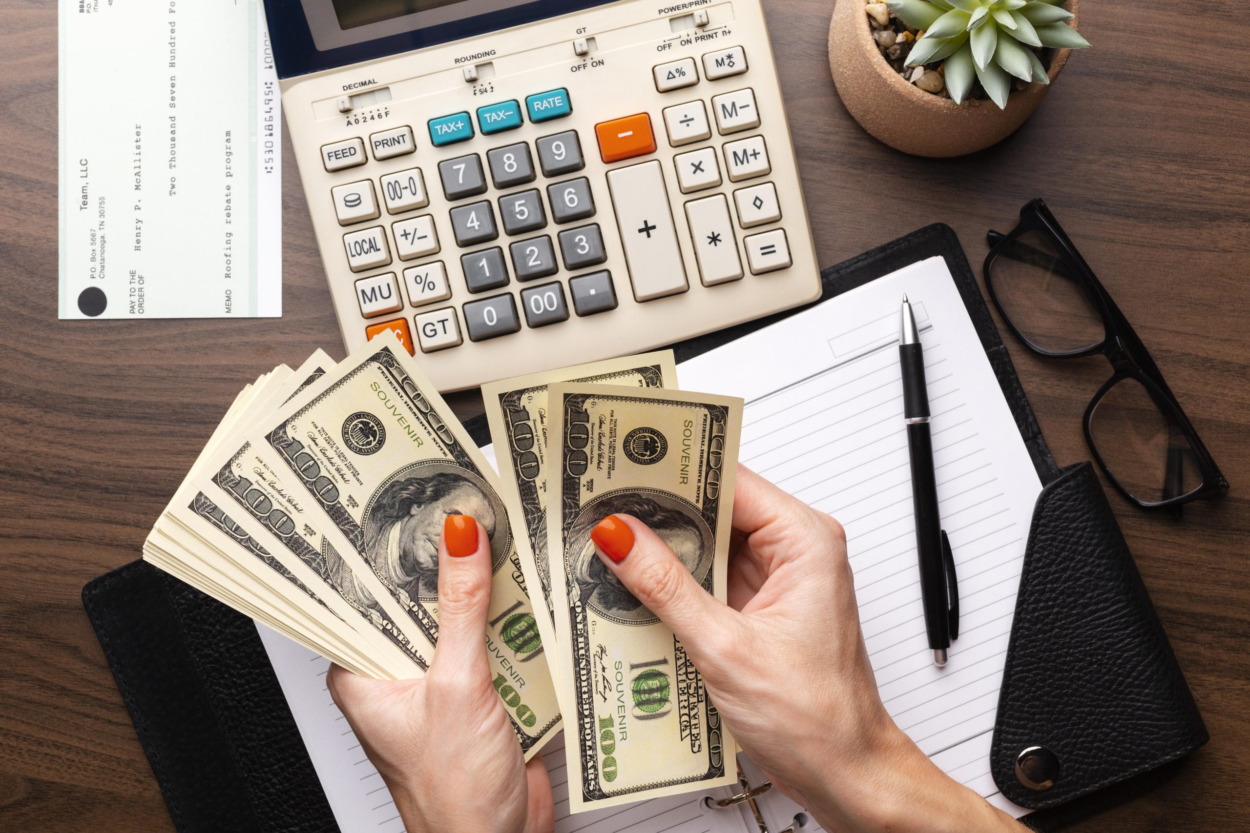 Close-up women's hands counting money with ledger and calculator in background.